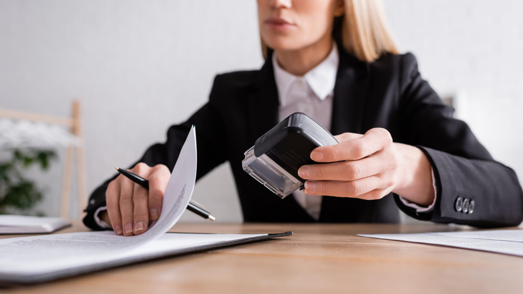 A woman in a business suit is holding a rubber stamp.