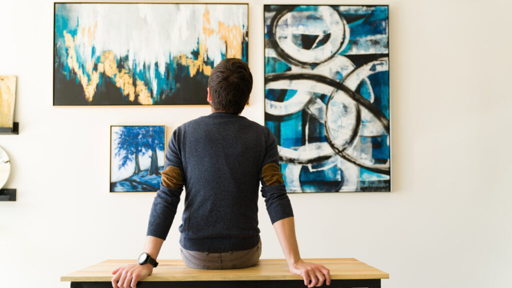 A man sitting at a table looking at art on the wall.