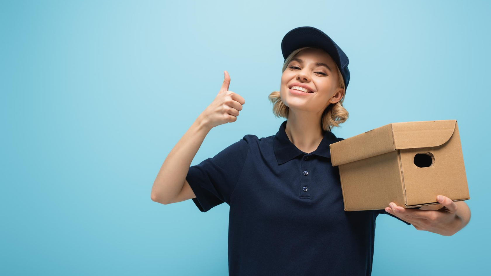 A woman holding a cardboard box and giving the thumbs up.